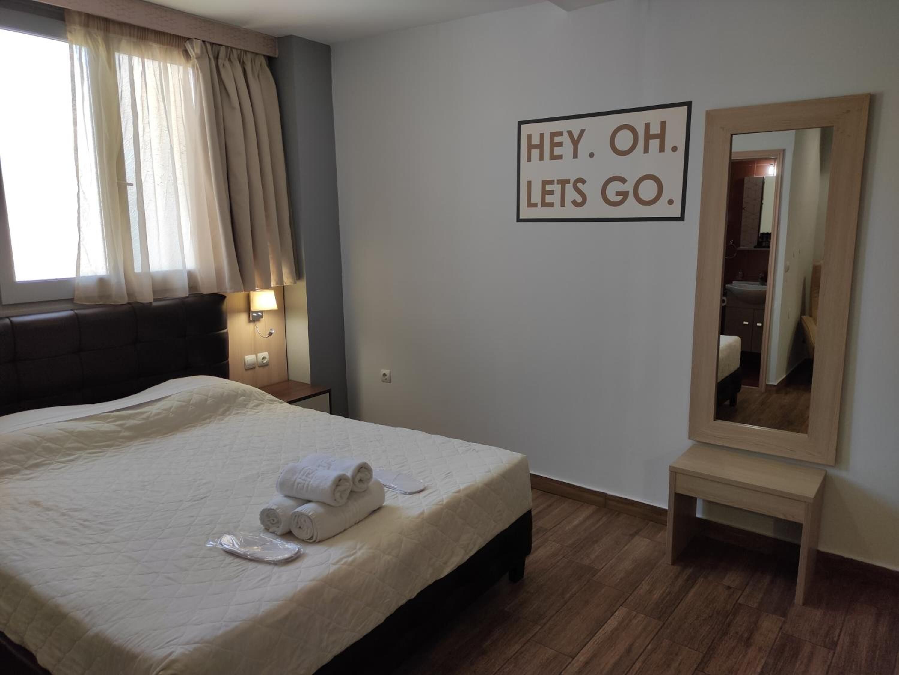Habitación de hotel con cama, mesita de noche con lámpara, espejo y cartel en la pared.
