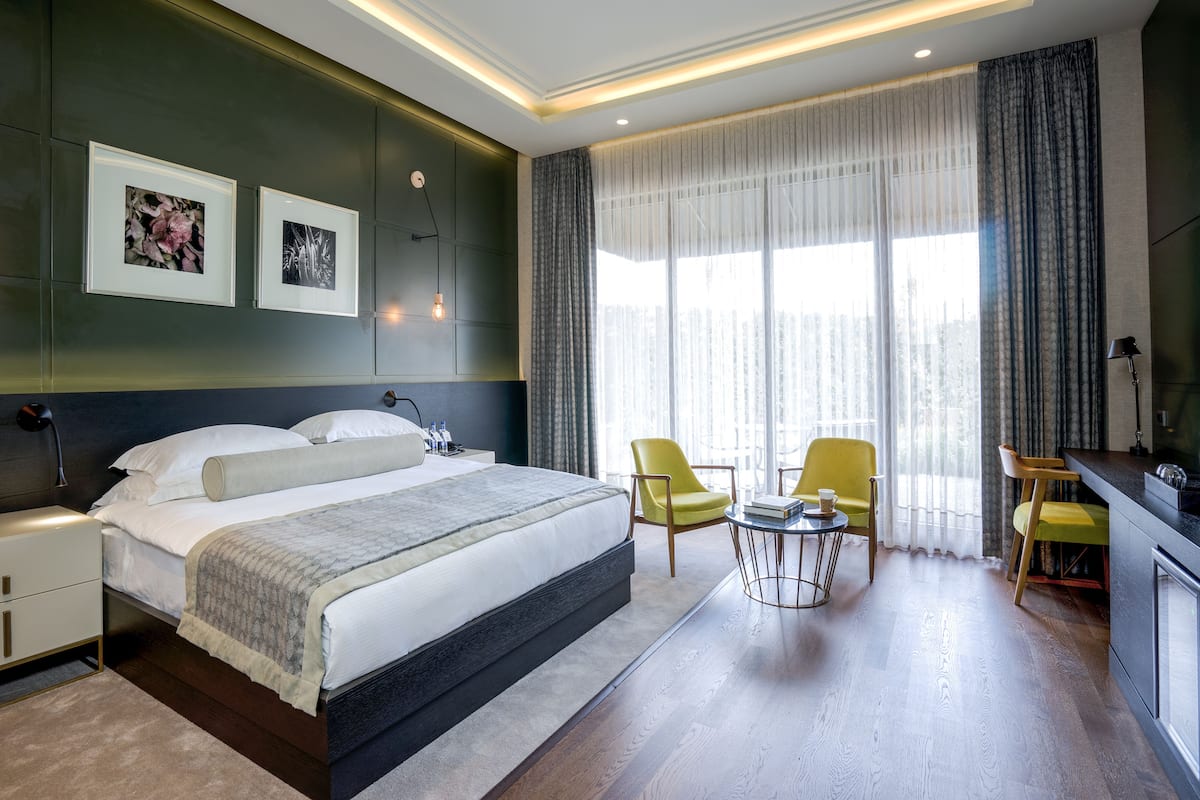 A modern hotel room with a large bed, two chairs, a small table, and a TV.