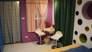 Una habitación con una cama, dos sillas, una mesita y un ventanal con cortinas.