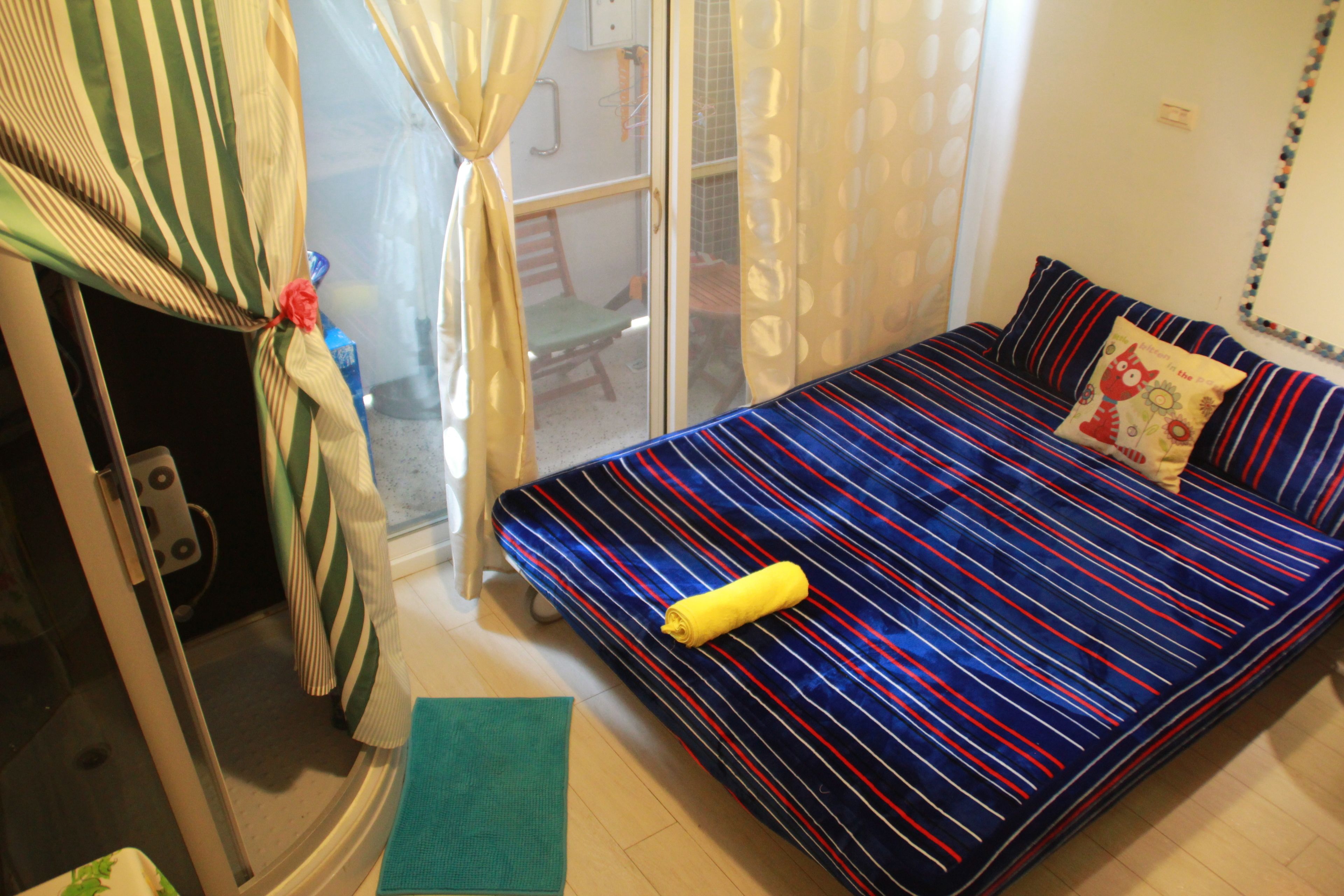 Una habitación con una cama, un tapete verde, una toalla amarilla y una ventana con cortinas.