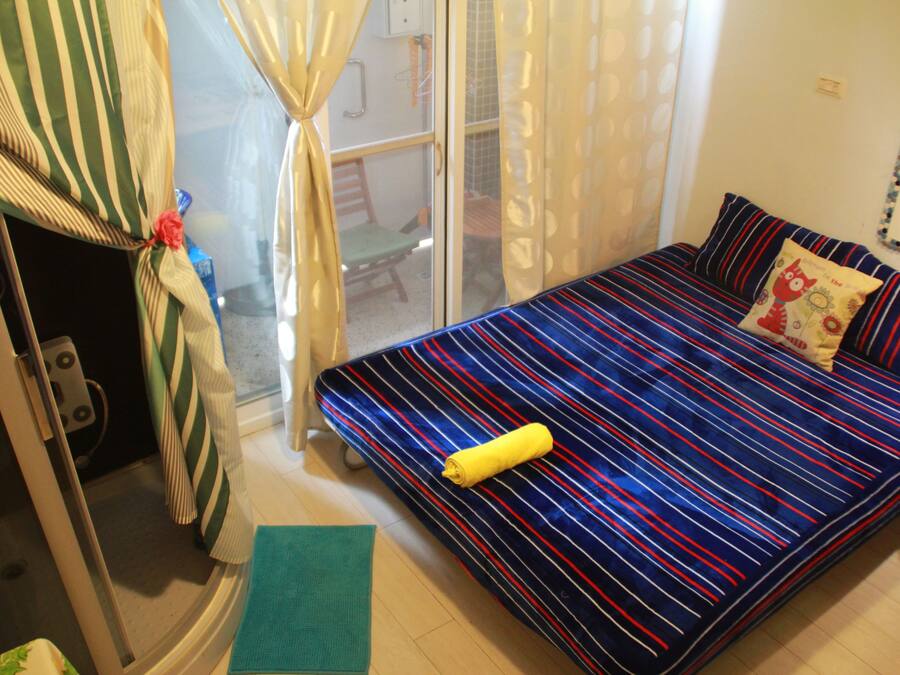 Una habitación con una cama, un tapete verde, una toalla amarilla y una ventana con cortinas.