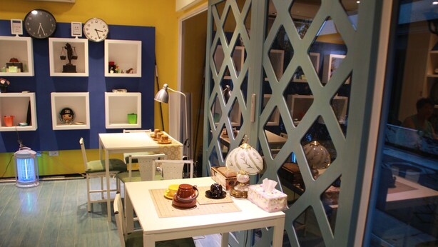 Una habitación con una mesa, sillas, una lámpara y estanterías con diversos objetos.
