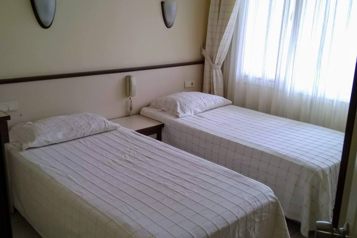 A hotel room with two beds, a telephone, an air conditioner, and a window with curtains.