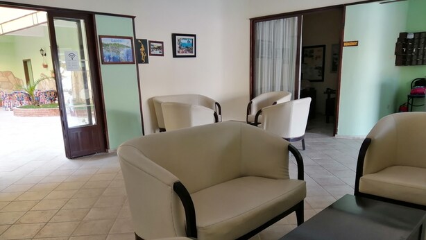 A hotel lobby with a seating area featuring sofas and a table, a glass door entrance, and framed pictures on the wall. - Oya Apartments (Kusadasi)