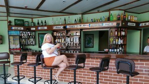 A bar area with a brick counter, multiple stools, and a variety of liquor bottles on shelves. - Oya Apartments (Kusadasi)