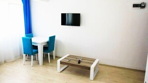 A small room with a white table and blue chairs, a wooden coffee table, a flat-screen TV mounted on the wall, and a light switch on the wall. - Mavi Butik Apart (Cesme)