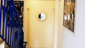 A staircase with blue railings leading to a room with a round mirror on the wall and a framed picture. - Mavi Butik Apart (Cesme)