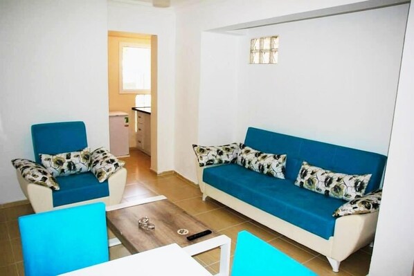 A living room with a blue sofa set, a coffee table, and a chair. - Mavi Hotels (Cesme)