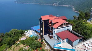 Un hotel con techo rojo, zona de piscina y vista al mar.