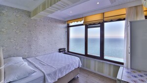 Un dormitorio con una cama, una silla, una mesita y una ventana con vista al mar.