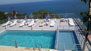 Un área de piscina con tumbonas y sombrillas, vista despejada al océano y un puesto de socorristas.
