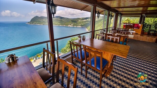 Un restaurante con vista al mar, mesas y sillas de madera, y piso a cuadros.
