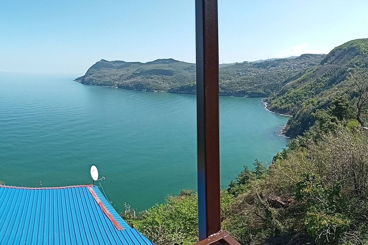 Vista desde un balcón sobre una extensa masa de agua, con una isla y colinas a lo lejos.
