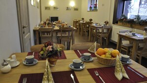 Een ontbijtruimte met meerdere tafels, voorzien van fruitmanden, bekers en netjes gepresenteerd bestek.