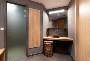 A modern bathroom with a wooden vanity, a glass door, and a woven trash bin. - Grand Apartments (Spindleruv Mlyn)