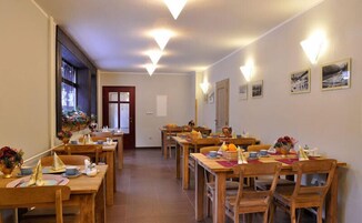 Un comedor con varias mesas y sillas de madera, una puerta al fondo, y lámparas fijadas a la pared.
