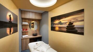 A spa room with a massage table, a wooden cabinet, a sink, and a painting of a sunset over water.