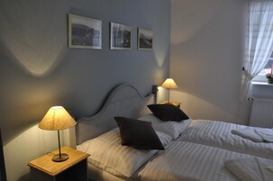Un dormitorio con dos camas, una mesita de noche con una lámpara y tres cuadros en la pared.