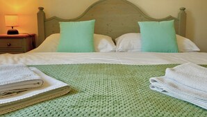Een netjes opgemaakt bed met een groen gebreid plaid, witte kussens en opgevouwen handdoeken op een houten hoofdbord.
