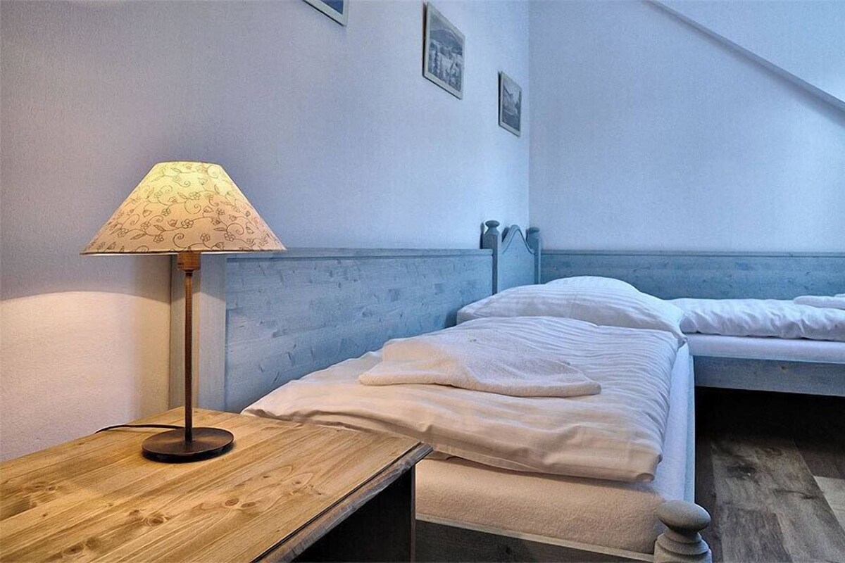 Un dormitorio con dos camas, una mesita de noche de madera, una lámpara y un cabecero fijado a la pared.