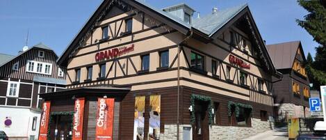 Un edificio tradicional con entramado de madera, con el letrero 'GRAND Hotel', varias pancartas y fachada de piedra.