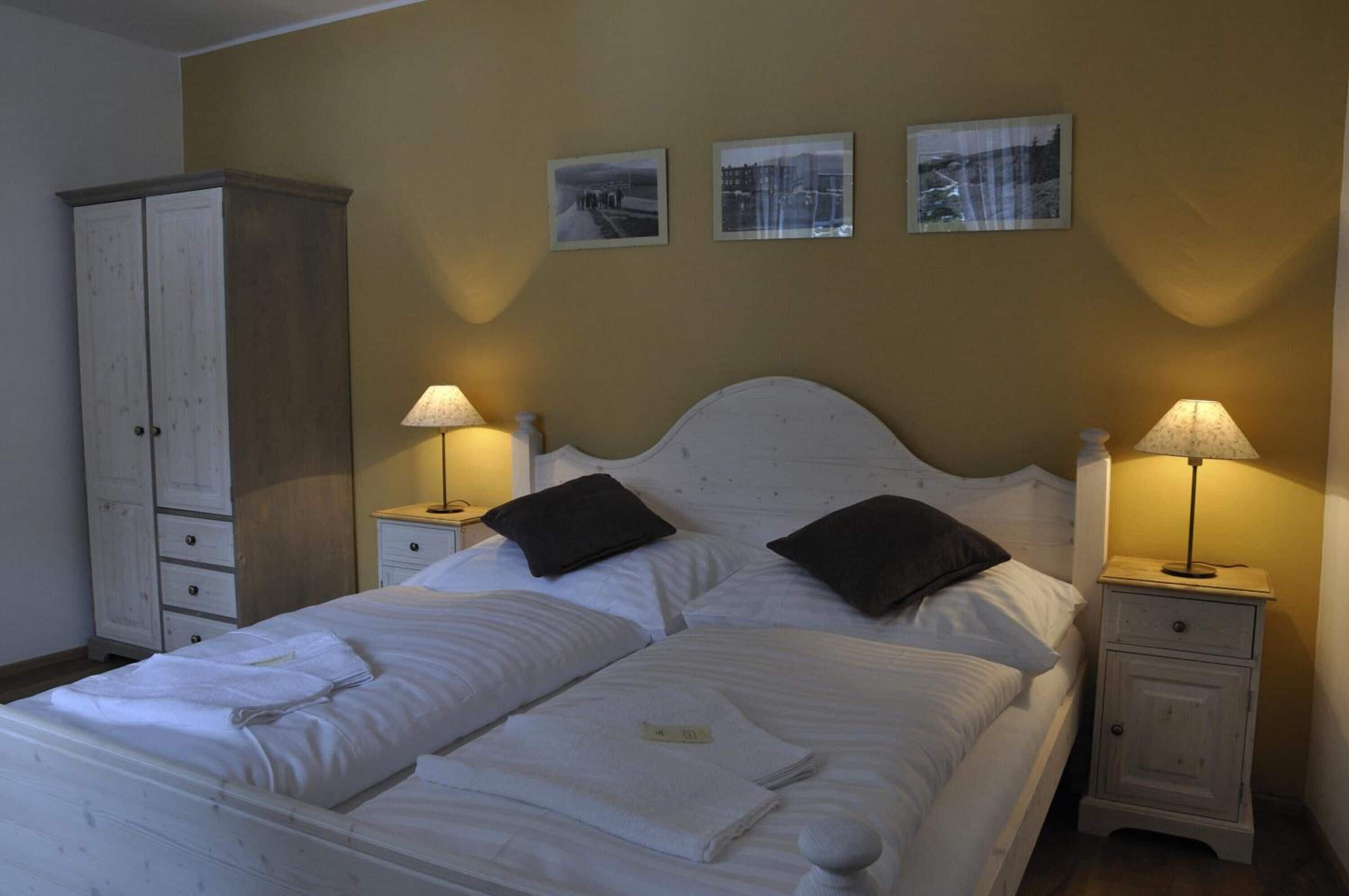 A neatly made bed with white linens, two bedside tables with lamps, and a wardrobe.