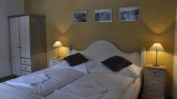 A neatly made bed with white linens, two bedside tables with lamps, and a wardrobe.