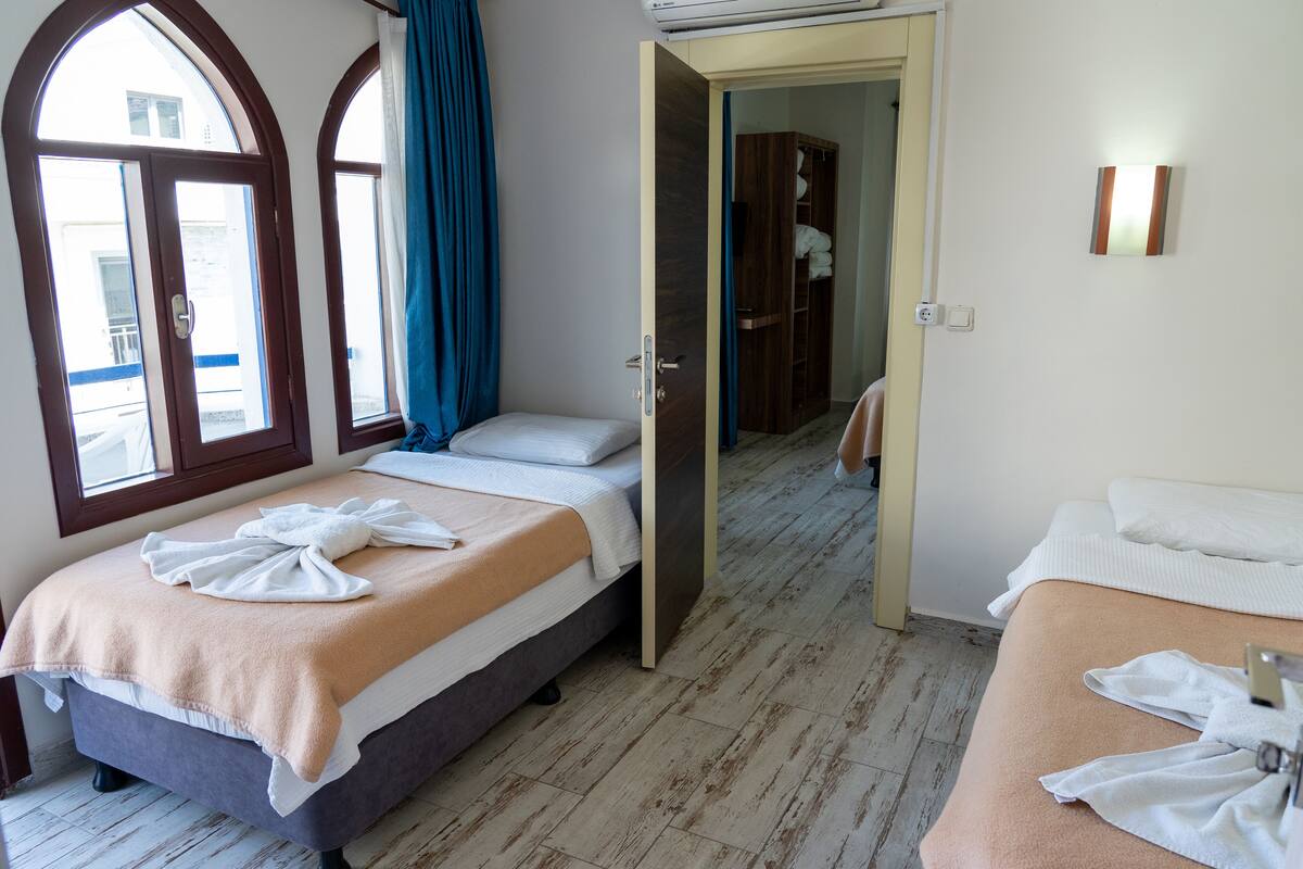 A hotel room with two beds, a wooden floor, and a view through an open door.
