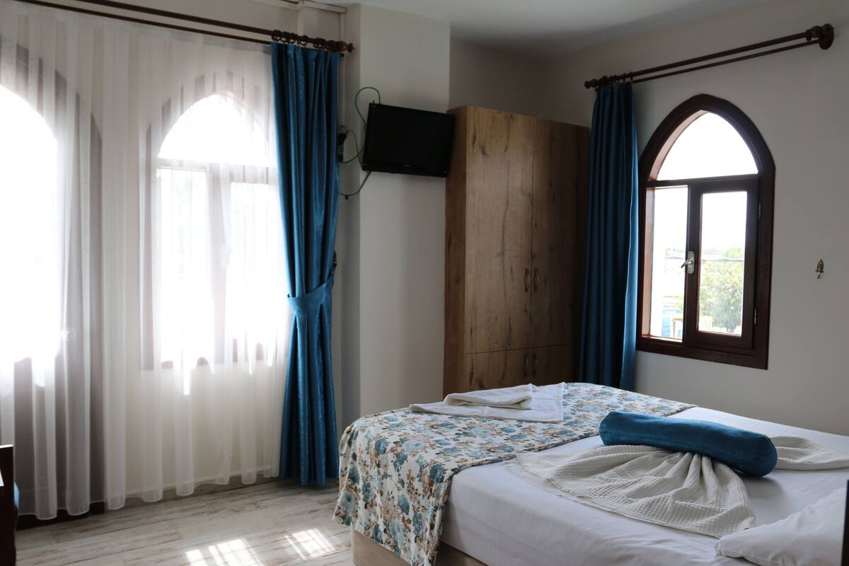 A bedroom with a bed, curtains, a wooden wardrobe, a television, and a window with an arched design.