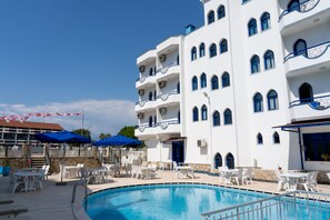 A hotel with a swimming pool, outdoor seating, and a white facade with blue accents. - Otel Eroglu (Fethiye)