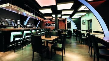 A modern bar area with a long counter, multiple seating options, and a unique ceiling design.