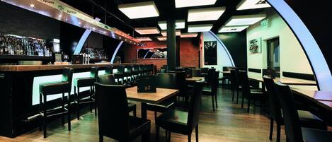 A modern bar area with a long counter, multiple seating options, and a unique ceiling design.
