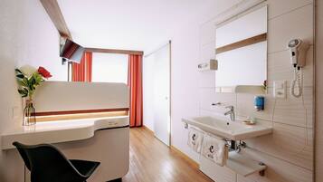 Een moderne badkamer met een wastafel, spiegel en haardroger. Er staat een stoel en een vaas met bloemen.
