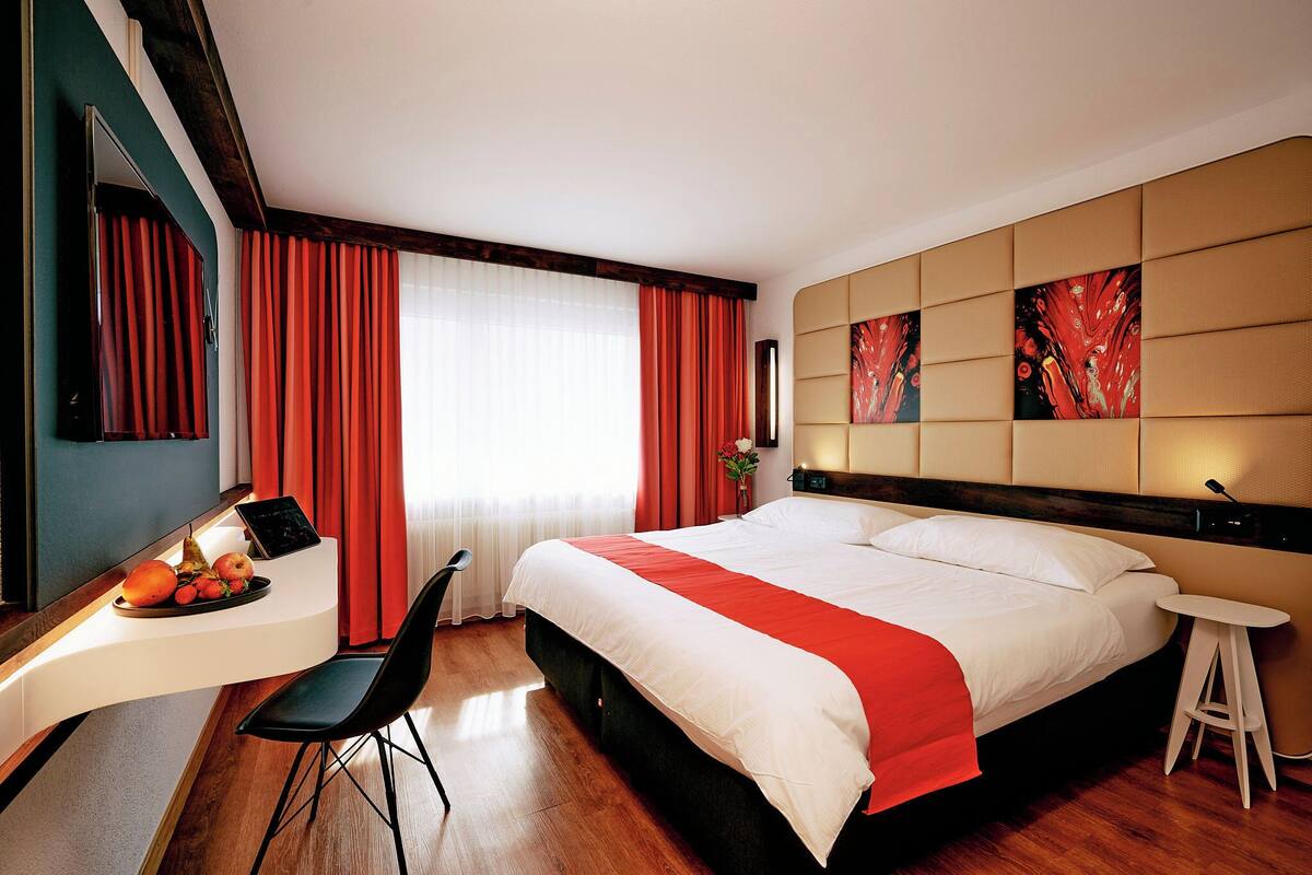 Ein Hotelzimmer mit einem Bett, einem Schreibtisch mit Computer, einem Stuhl und einem kleinen Hocker.