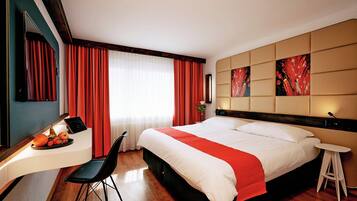A hotel room with a bed, a desk with a computer, a chair, and a small stool.