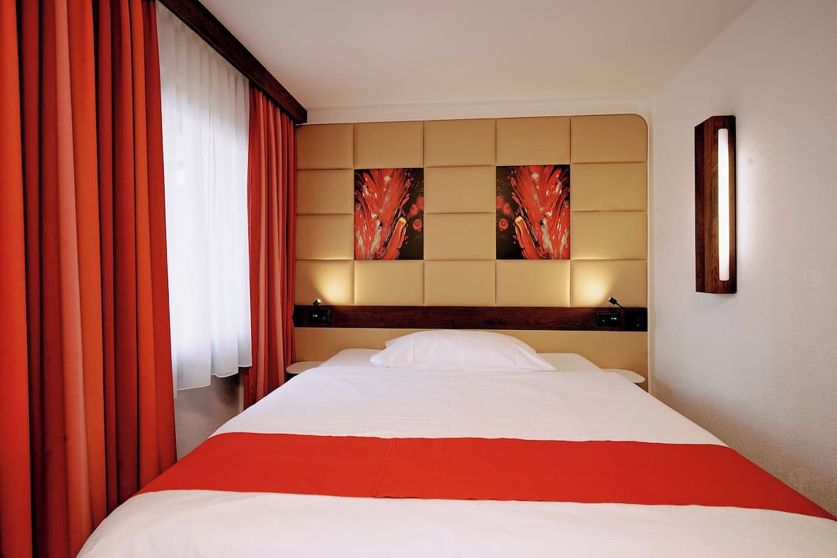 Ein Hotelzimmer mit einem großen Bett, roten Vorhängen und zwei Kunstwerken an der Wand.