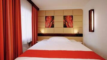 Una habitación de hotel con una cama grande, cortinas rojas y dos obras de arte colgadas en la pared.