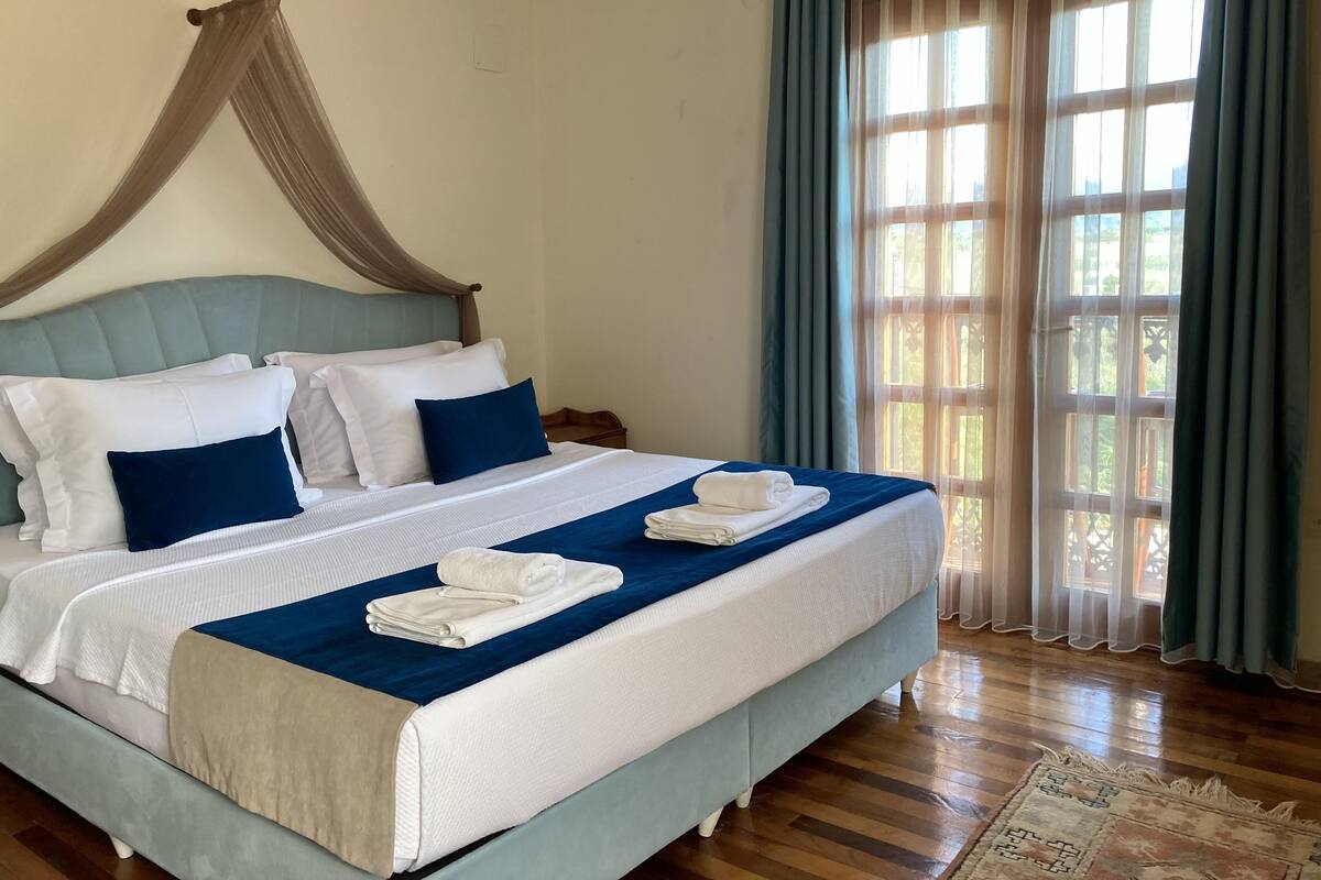 A large bed with a canopy, white and blue bedding, and neatly folded towels.