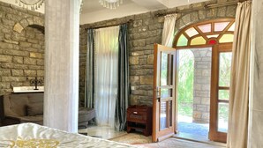 A bedroom with a large bed, stone walls, a wooden door leading outside, and a small table with a candle. - Portofino Boutique Hotel (Ula)