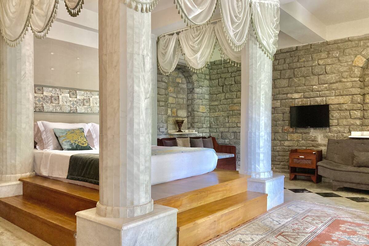 A bedroom with a stone wall, a bed, a sofa, and a TV.