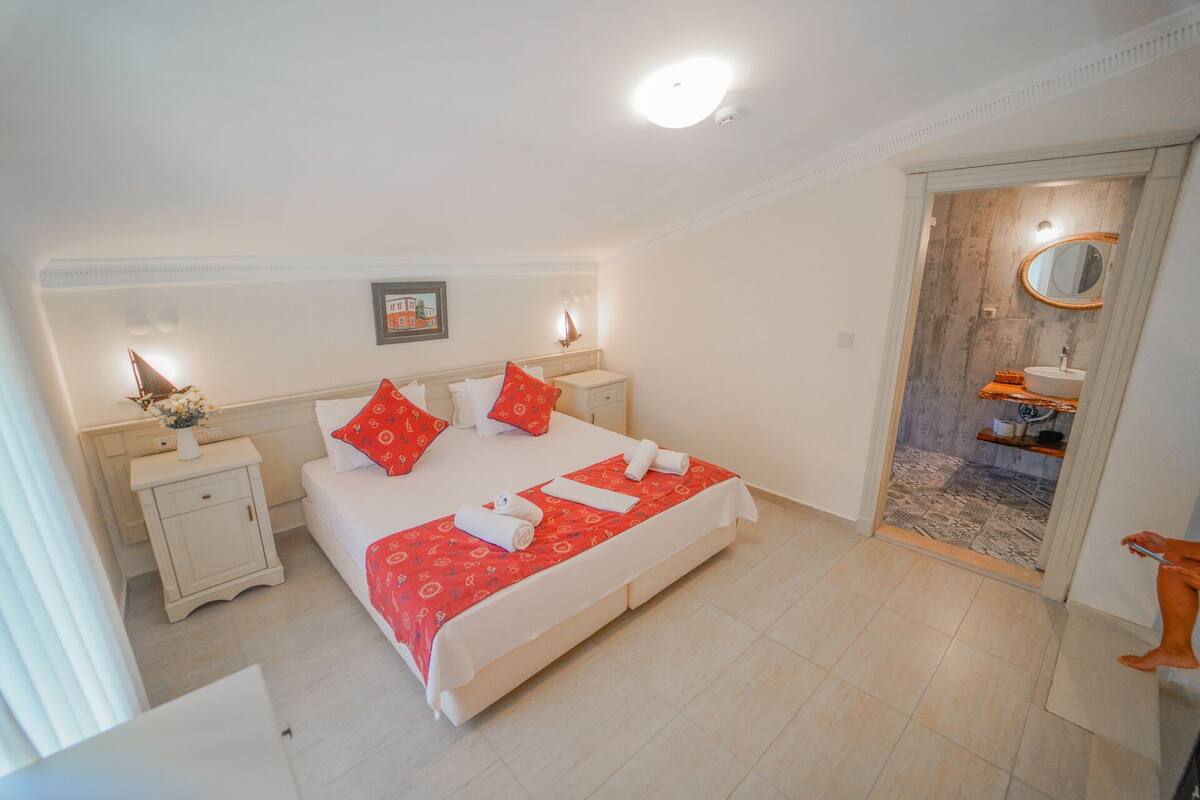 Ein Hotelzimmer mit einem großen Bett, zwei Nachttischen, einem Spiegel und einem durchgegangene Tür sichtbaren Badezimmer.