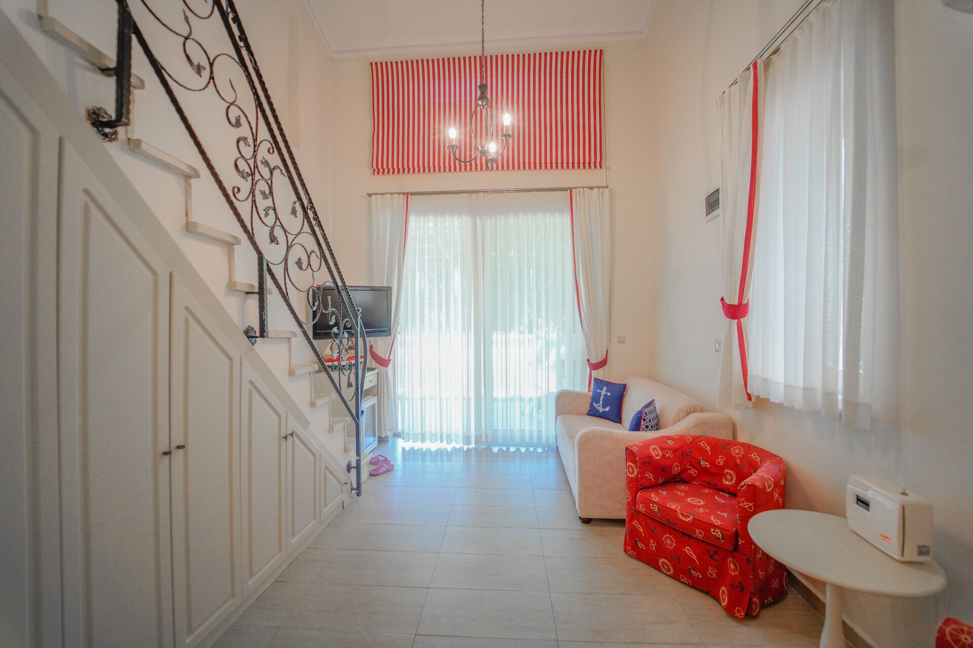A hallway with a staircase, a living area with a sofa and a red patterned chair, and a small table.