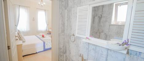 Un baño con pared de mármol, un lavabo blanco y un espejo encima.