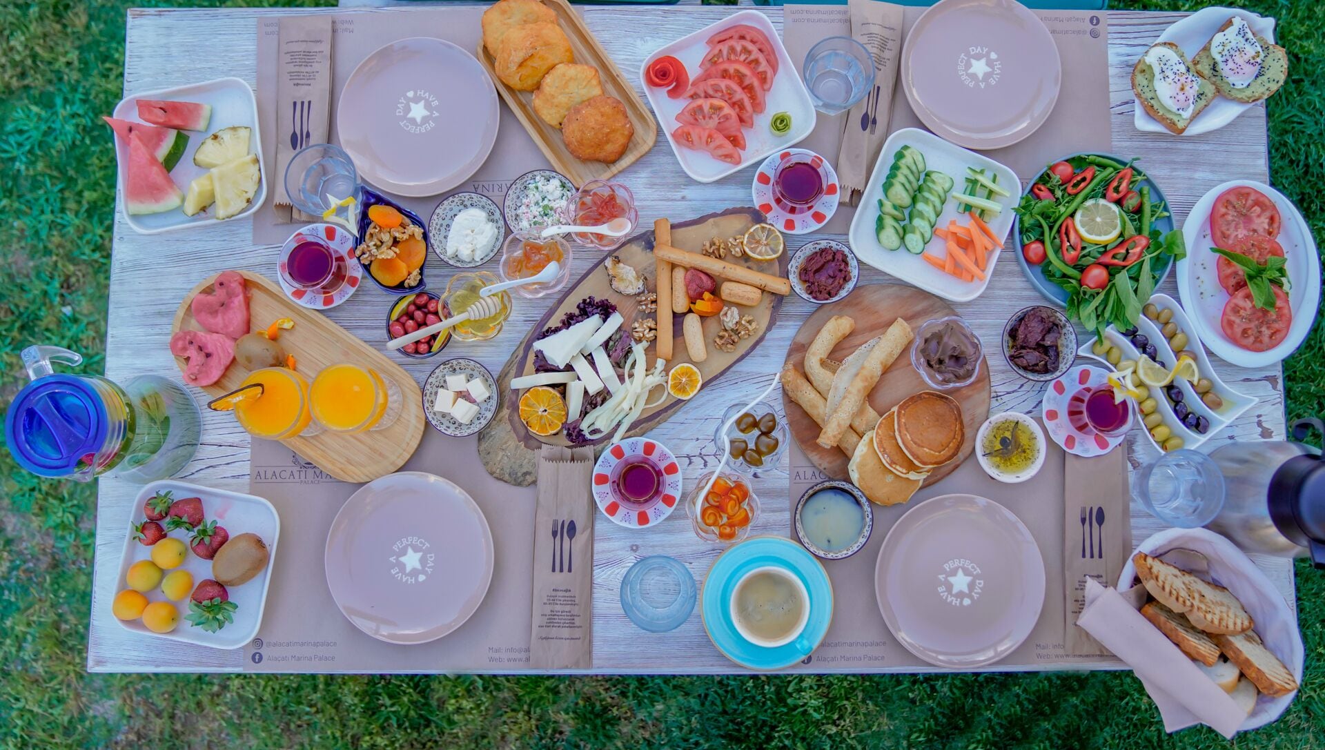 A picnic setup with various food items and drinks spread across a table outdoors.