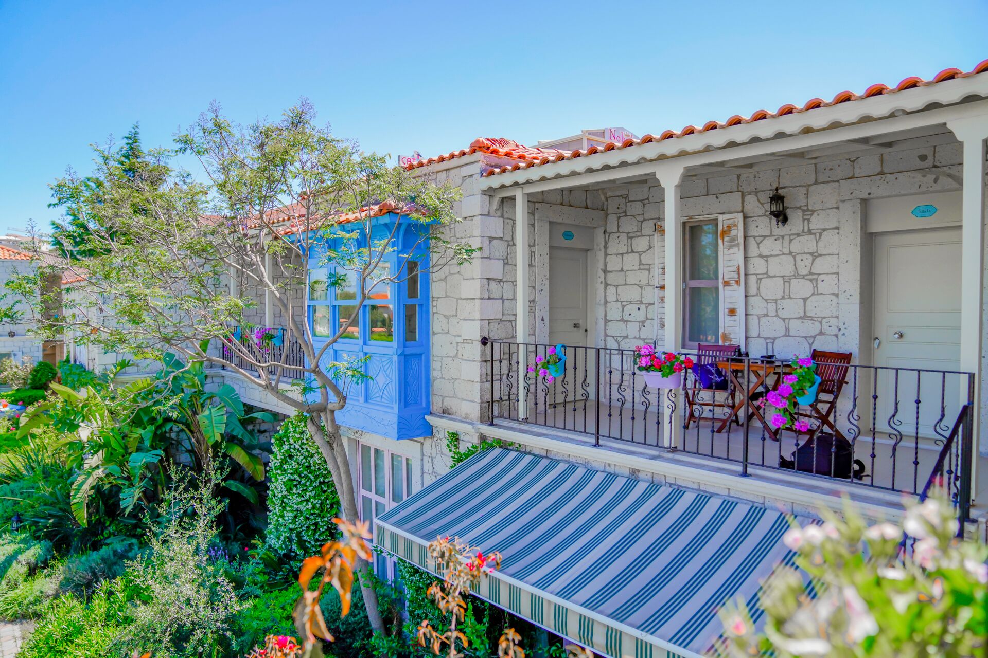 A traditional stone building with a blue door and a covered balcony with chairs and potted plants.