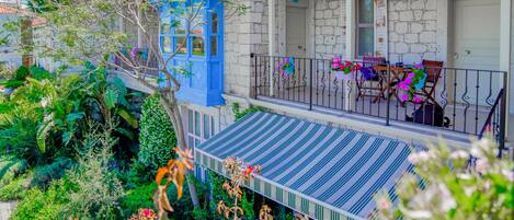 A traditional stone building with a blue door and a covered balcony with chairs and potted plants.