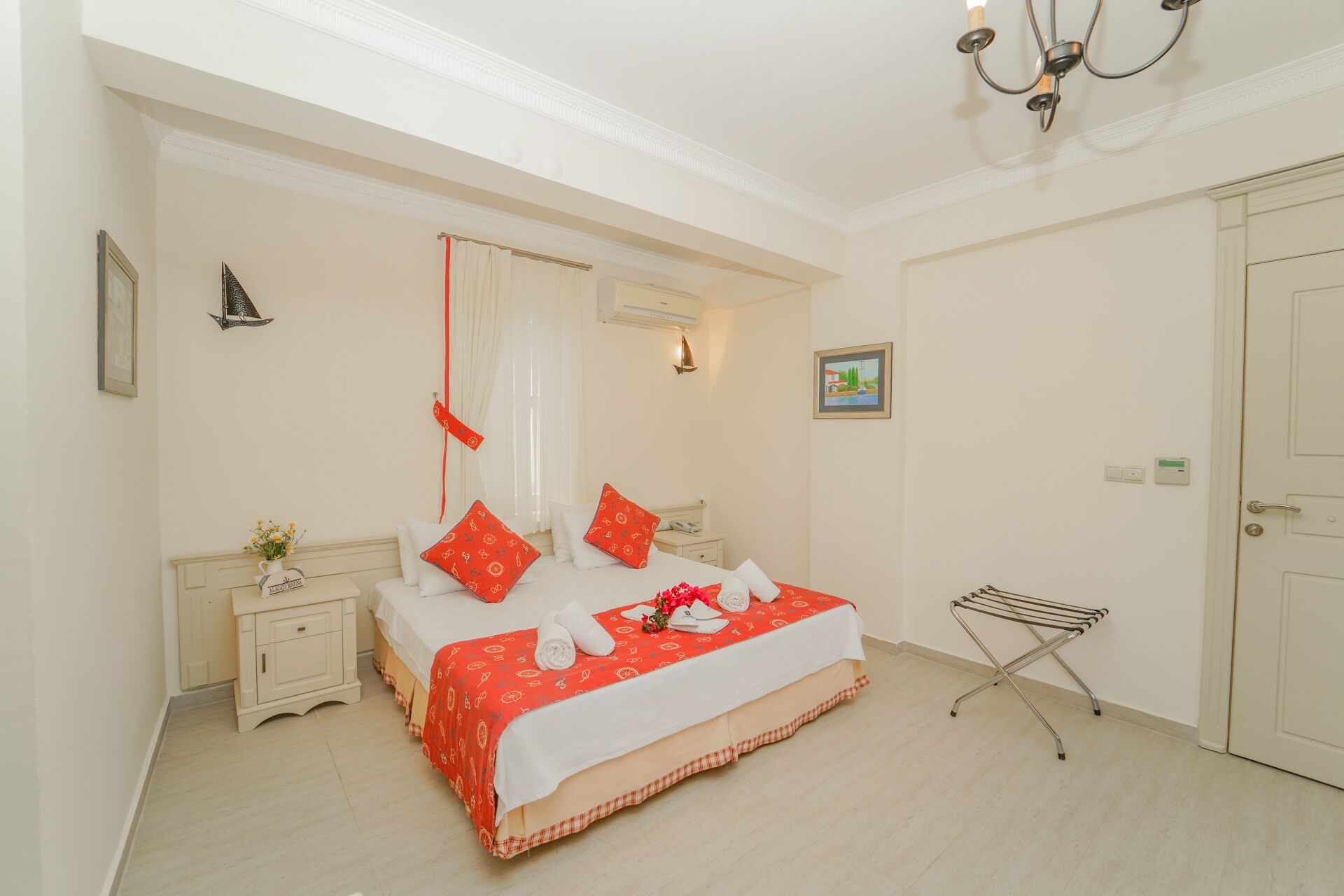 Habitación de hotel con cama, mesita de noche, lámpara de pared, ventana con cortinas, puerta y aire acondicionado instalado en la pared.