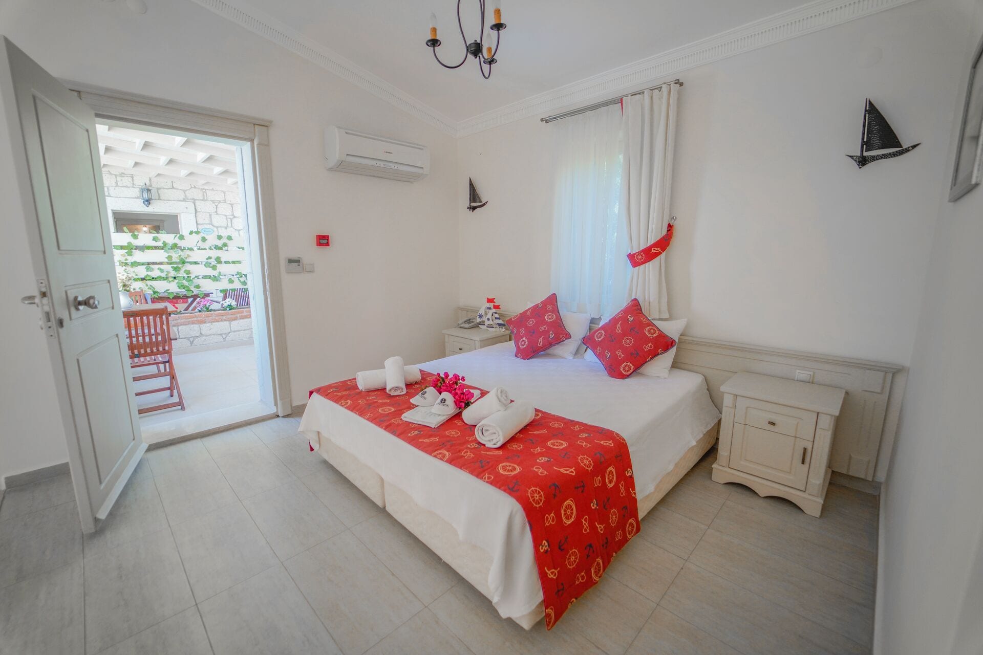 Quarto de hotel com uma cama grande, uma mesa de cabeceira, cortinas em uma janela, um aparelho de ar condicionado e uma porta que dá para uma área externa.