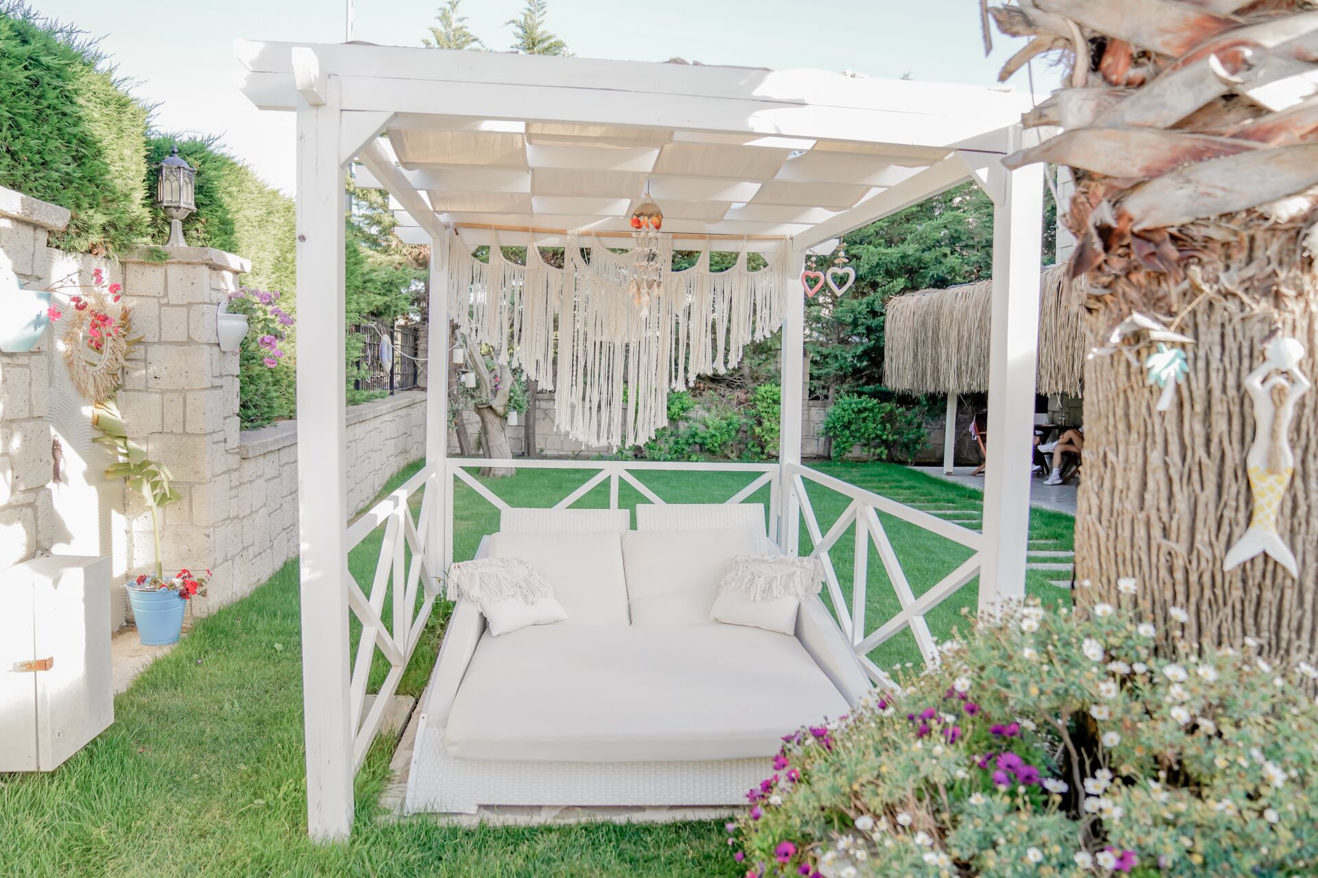 A white outdoor seating area with a canopy, surrounded by greenery and decorative elements.