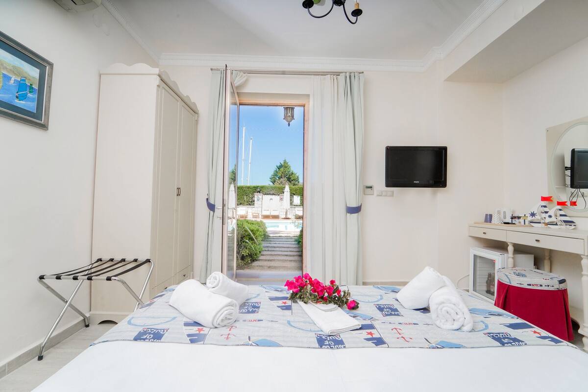 Ein Hotelzimmer mit Bett, Fernseher, Schreibtisch und Blick auf einen Pool sowie umliegende Gebäude.